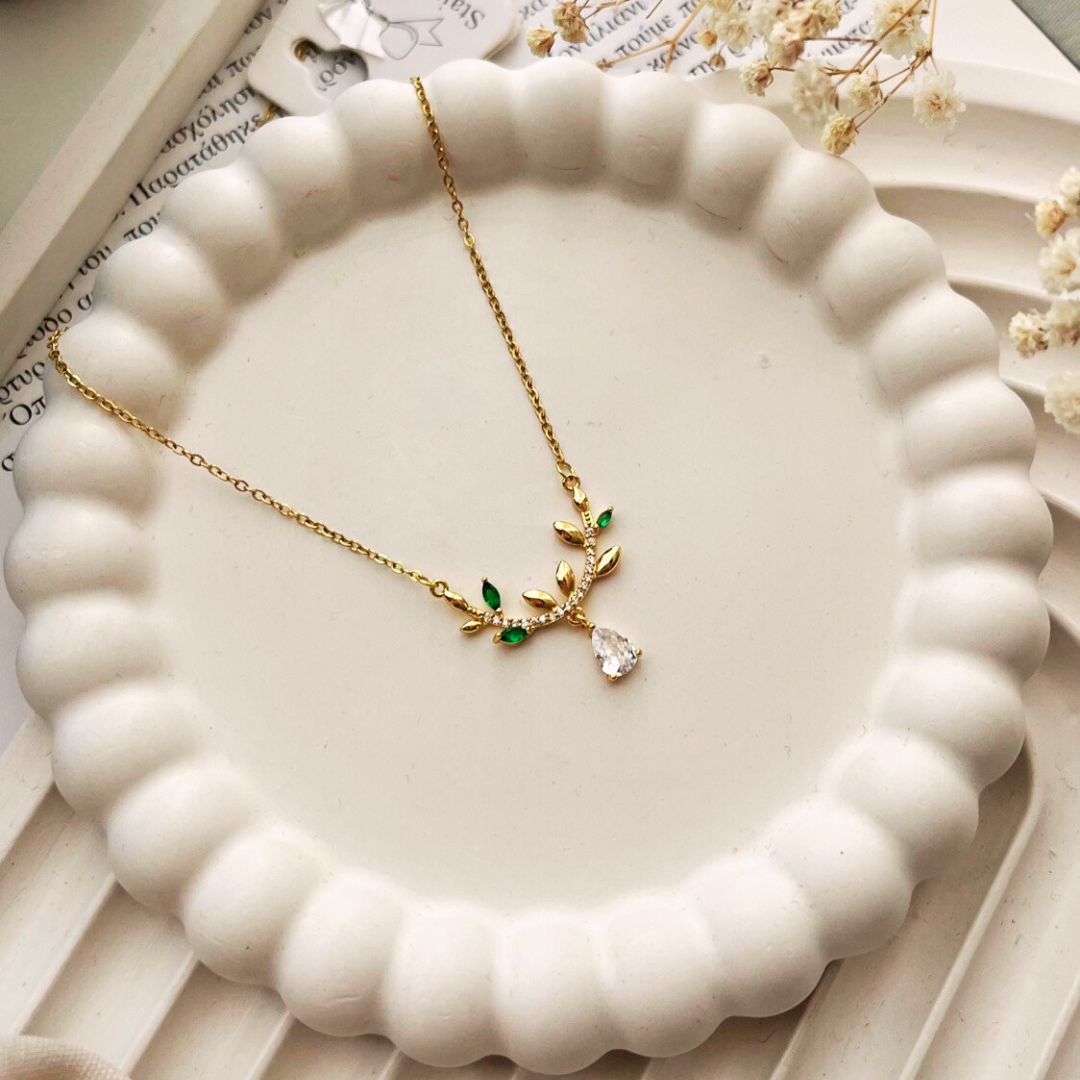 Gold necklace with green and clear stones on a white ceramic dish