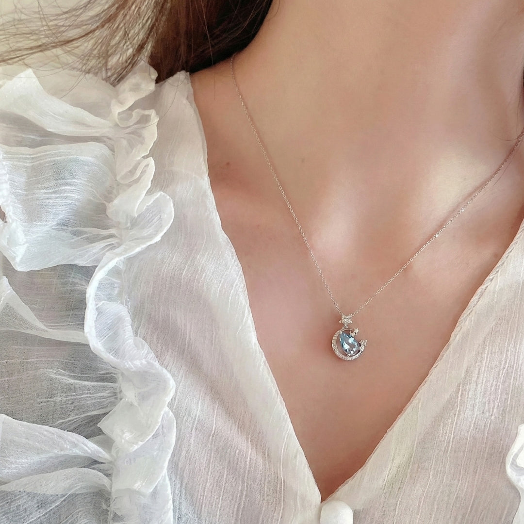 The Moondust Whisper Necklace captures the ethereal beauty of a moonlit sky, featuring a mesmerizing blue water-drop stone nestled within a delicate celestial crescent. It brings a sophisticated sense of wonder to any look.